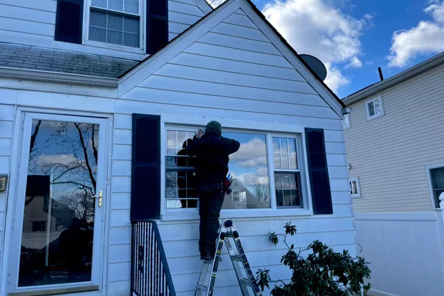 A man on a ladder carefully painting the windows of a house, showcasing his attention to detail and craftsmanship.